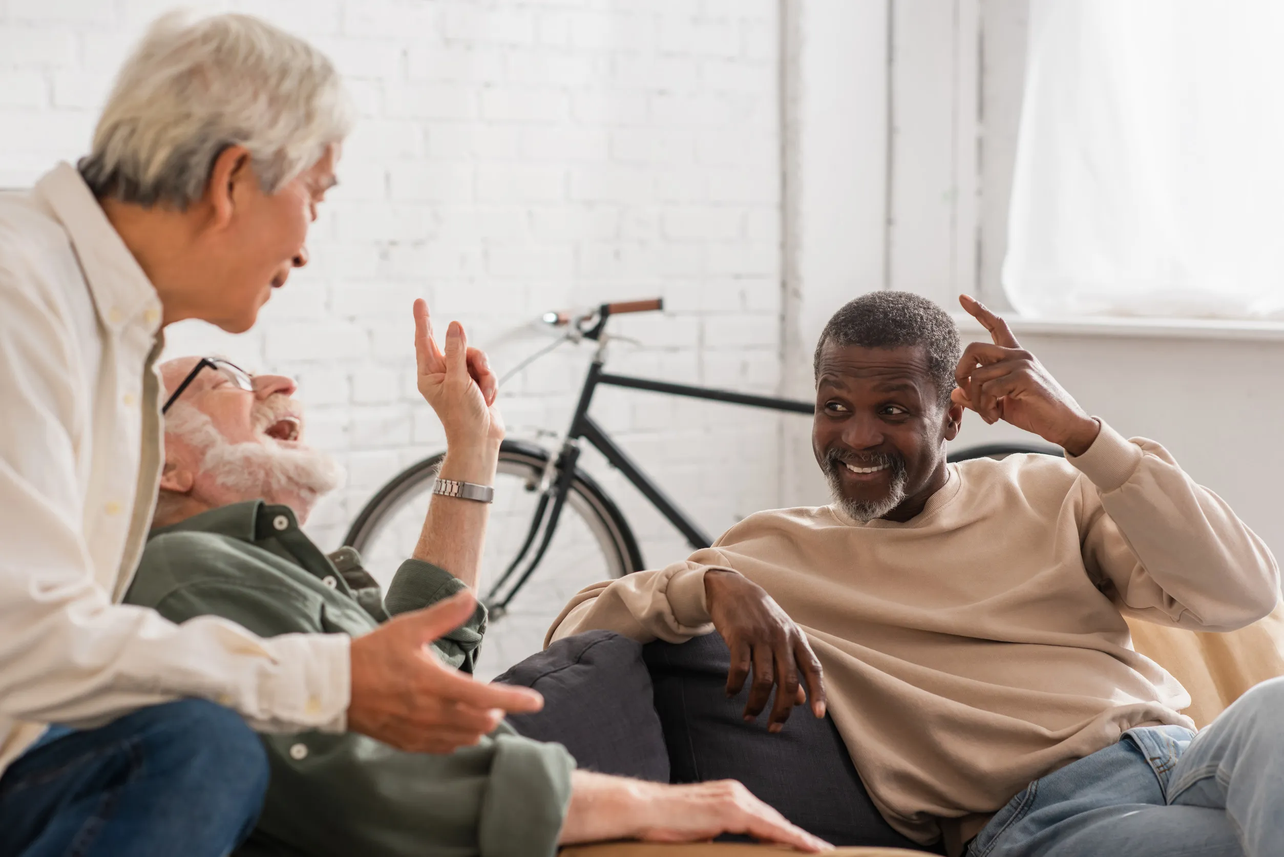 Cheerful multicultural elderly men talking on couch at home Cheerful multicultural elderly men talking on couch at home